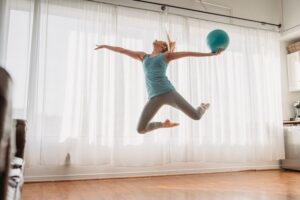 Slim woman in sportswear jumping up with ball