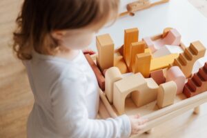 Unrecognizable little girl playing with wooden blocks at table at home